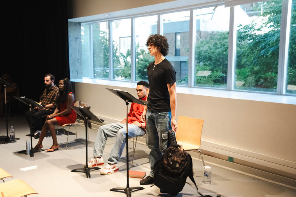 An actor stands in front a of music stand.